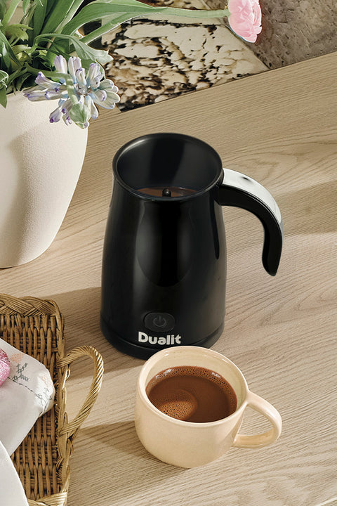                                                                             Black Dualit coffee maker utensil on a wooden table with a beige mug of coffee.                                                                      